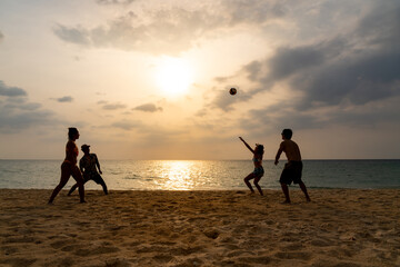 Group of Asian man and woman friends playing beach volleyball together on tropical beach in sunny day. Male and female friendship enjoy and having fun outdoor lifestyle activity on summer vacation