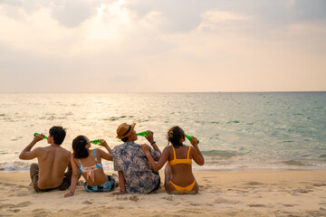 Fototapeta na wymiar Group of Happy Asian man and woman friends sitting on the beach enjoy drinking beer with talking together at summer sunset. Male and female friendship relax and having fun outdoor lifestyle activity.