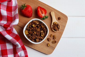 A bowl of granola with strawberries, on a wooden board . Delicious breakfast, morning concept. Healthy food. Flat lay, top view