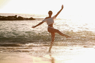 Fototapeta na wymiar Beautiful caucasian woman playing in the water on the sandy beach at sunset sea shore.