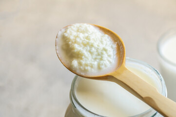 Kefir grains in wooden spoon with glass of kefir drink, healthy fermented probiotic cold dairy drink