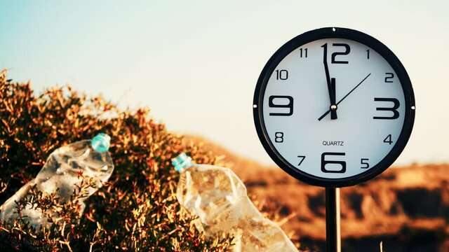 Time is running out. Clock ticking showing twelve o' clock. Plastic water bottle abandoned on nature. Environmental pollution global ecological problem.