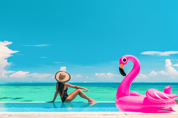 Vacation summer fun woman sunbathing with inflatable pink flamingo pool float by infinity swimming pool. Luxury travel holiday at overwater villa resort. © Maridav