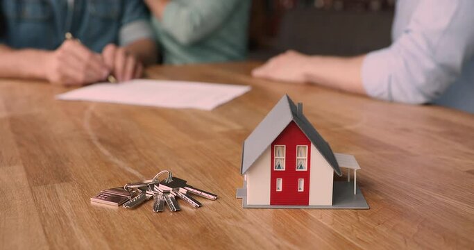 Bunch of keys and cottage house toy model on wooden table close up view, couple sign bank loan agreement or real estate rental contract, closing deal with handshake on background. Buy property concept
