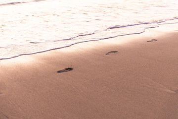 Footprints in the sand by the sea. In the light of the sunset, the footprints follow the sand along the surf.