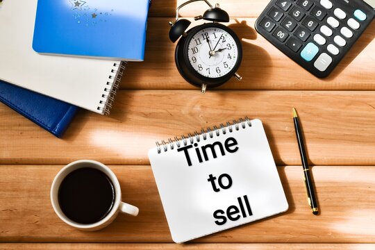 TIME TO SELL text in a notepad near a calculator, alarm clock and a cup coffee, clipboard on a wooden background. Business concept. Flat lay.