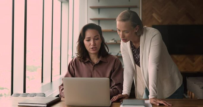 Female colleagues using laptop work together on collaborative task. Mentor provide help, share skills help with corporate software app to trainee new company employee. Apprenticeship, teamwork concept