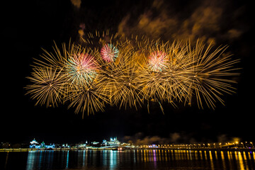 bright festive fireworks with beautiful flowers bloom over the river on a warm clear evening