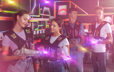 Two young girls talking and holding guns during laser tag game with men in dark labyrinth