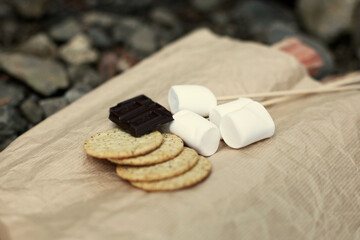 a piece of chocolate, graham crackers, and marshmallows on the brown paper for preparing for s'more