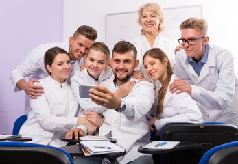 Positive students of medical faculty with female teacher making selfie indoors