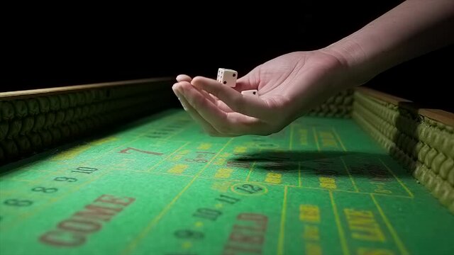 This video shows an anonymous hand shaking a pair of dice and rolling them towards the camera on a green felt craps gambling table in slow motion.