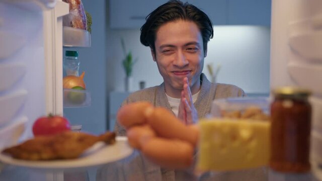 Sleepy hangry man in bathrobe at midnight opening refrigerator and taking all food, gluttony. Unhealthy lifestyle concept