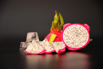 Ripe tropical fruit Pitaya, cut into pieces and cubes of melted ice on a black background.