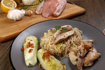 Asian western fusion fried noodles sliced chicken breast thyme garlic ginger chilli Chinese cabbage onion lemon served on grey plate chopsticks soya sauce on wooden table raw ingredients