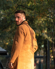 Fototapeta premium Fall portrait of a bearded man with a brown coat at sunset time in the park