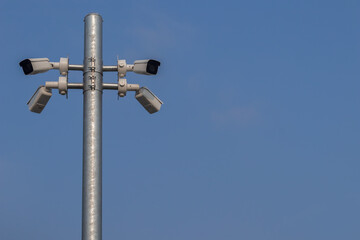 Low angle view of the surveillance security cameras on steel pole in outdoor public car parking with clear blue sky background.