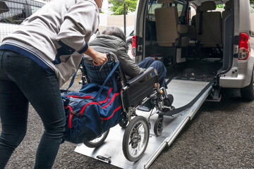 デイサービスの送迎車に乗せられる高齢者の女性。 An elderly woman in a car to go to a day care facility.	