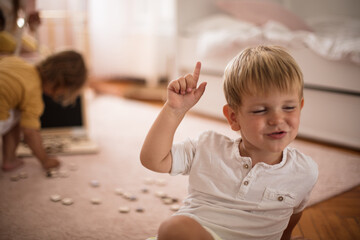 Little boy with finger up at home. Sitting in room.