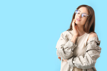 Young woman wearing eyeglasses on color background