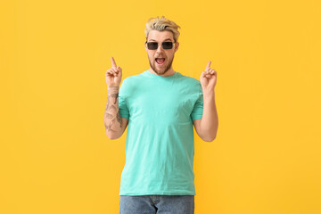 Young man with stylish sunglasses pointing at something on color background