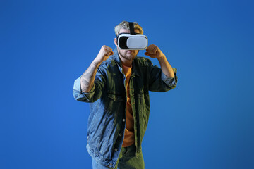 Young man with VR glasses on color background