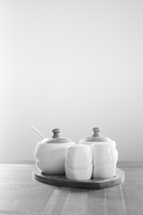 Monochrome seasoning containers of a table. Creative kitchenware photography. Sugar, pepper and salt. Selective focus on wooden details, blurred background.