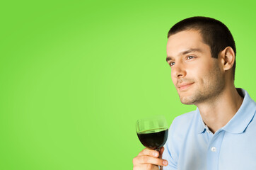 Portrait of thinking man with glass of wine, looking forward, isolated over green color background with copy space for some slogan or text.
