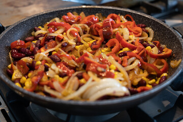 Mexican style stir fry, in a non stick pan on gas stove. The food inside the pan is with bell pepper, corn, unions and kidney beans.