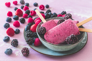 Homemade mixed berry yogurt ice popsicles in a bowl on pink background