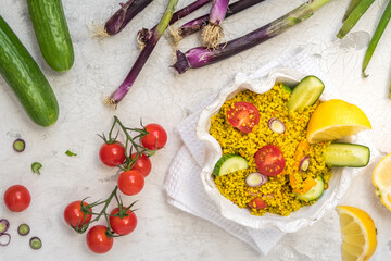 Healthy couscous salad with cucumber, tomatoes and onions in a white bowl on white background, decorated with colorful vegetables, top view