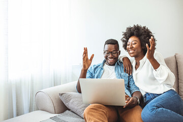 Shot of a young woman hugging her husband while he uses a laptop on the sofa at home. Wireless entertainment for a lazy day at home. Couple looking at laptop together in their cozy loft apartment