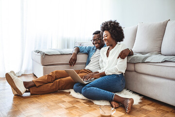 Young black couple sit on the floor using laptop, side view. People, leisure, mutliethnic...