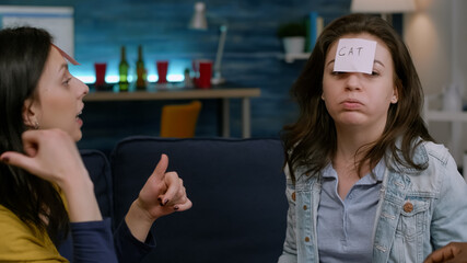 Group of multi-ethnic people enjoying spending time together while playing entertainment guess who game putting sticky notes on forehead. Happy friends laughing late at night