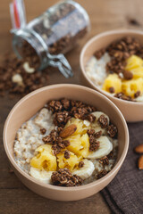 Oatmeal with pineapple, banana and chocolate granola in beige plates on a brown wooden table. A hearty healthy breakfast. Vertical photo