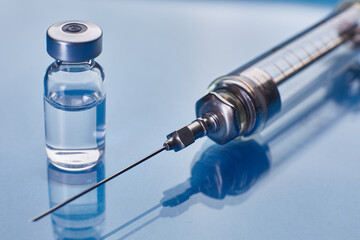 Glass vaccine vial and glass syringe on blue glass background