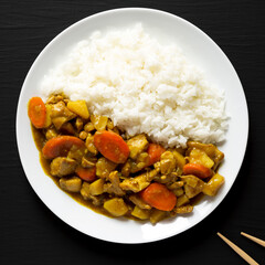 Homemade Japanese Chicken Curry  on a white plate on a black background, top view. Flat lay, overhead, from above.