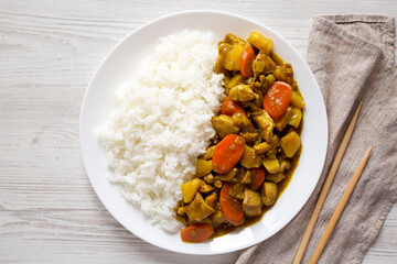 Homemade Japanese Chicken Curry  on a white plate on a white wooden surface, top view. Flat lay, overhead, from above.