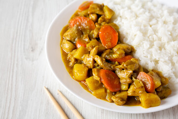 Homemade Japanese Chicken Curry  on a white plate on a white wooden background, side view. Copy space.