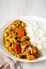 Homemade Japanese Chicken Curry  on a white plate on a white wooden background, side view. Space for text.