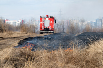 Burning vegetation in the meadows under the control of the fire department near the city - 433180170