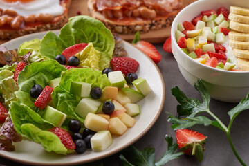 variety of open sandwiches made of brown whole wheat  bread with tomatoes sauce, bowl of oat granola with yogurt, white beans, bacon, fried egg. fresh fruit and vegetable salad, healthy breakfast.