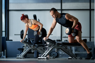 Fototapeta na wymiar Athletic couple having weight training on a bench while exercising in a gym.