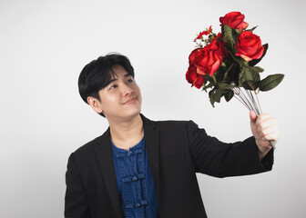 Young handsome Asian man in a suit on a white background holds a red rose. Romantic ideas and Marriage.