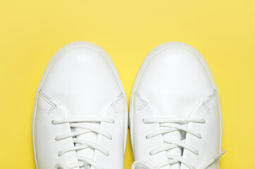 White sneakers on yellow background top view flat lay. Stylish youth women's leather sneakers, sports shoes, genuine leather footwear. Minimalistic shoe store advertising fashion style Shoe background
