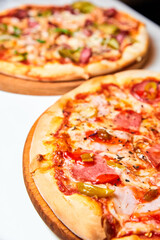 Pizza with salami, bell pepper, tomatoes and cheese, pickles, bacon and sausages on a light background. Close-up, selective focus