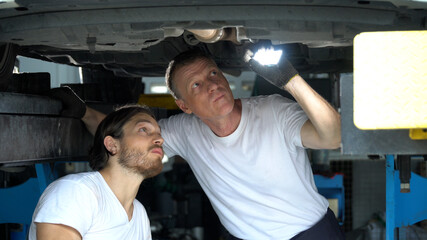two mechanic using flashlight   inspection to undercarriage of car in workshop at auto car repair service center with lifted vehicle  . group of car engineer team checking list vehicle details