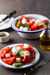 Healthy salad made from  vegetable feta cheese, cucumber, tomato, sweet pepper   and dressing with olive oil and spices in rustic bowl on dark concrete background