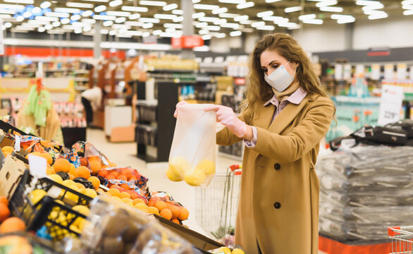 A young woman in a disposable mask and gloves buys fruits in a supermarket. Shopping during the lockdown and the Covid-19 coronavirus pandemic. Limiting the spread of infection