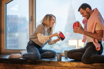 Young couple man and woman sitting at the window eating Asian food from a box of chopsticks and talking laughing, food delivery service